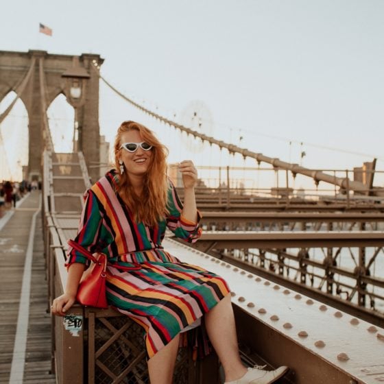 Woman in a rainbow Outfit sitting on the Brooklyn Bridge.